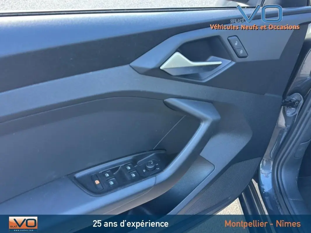 Vue rapprochée de la porte avant gauche gris foncé d'une Audi A1 Sportback 2020 avec commandes électriques et poignée argentée.