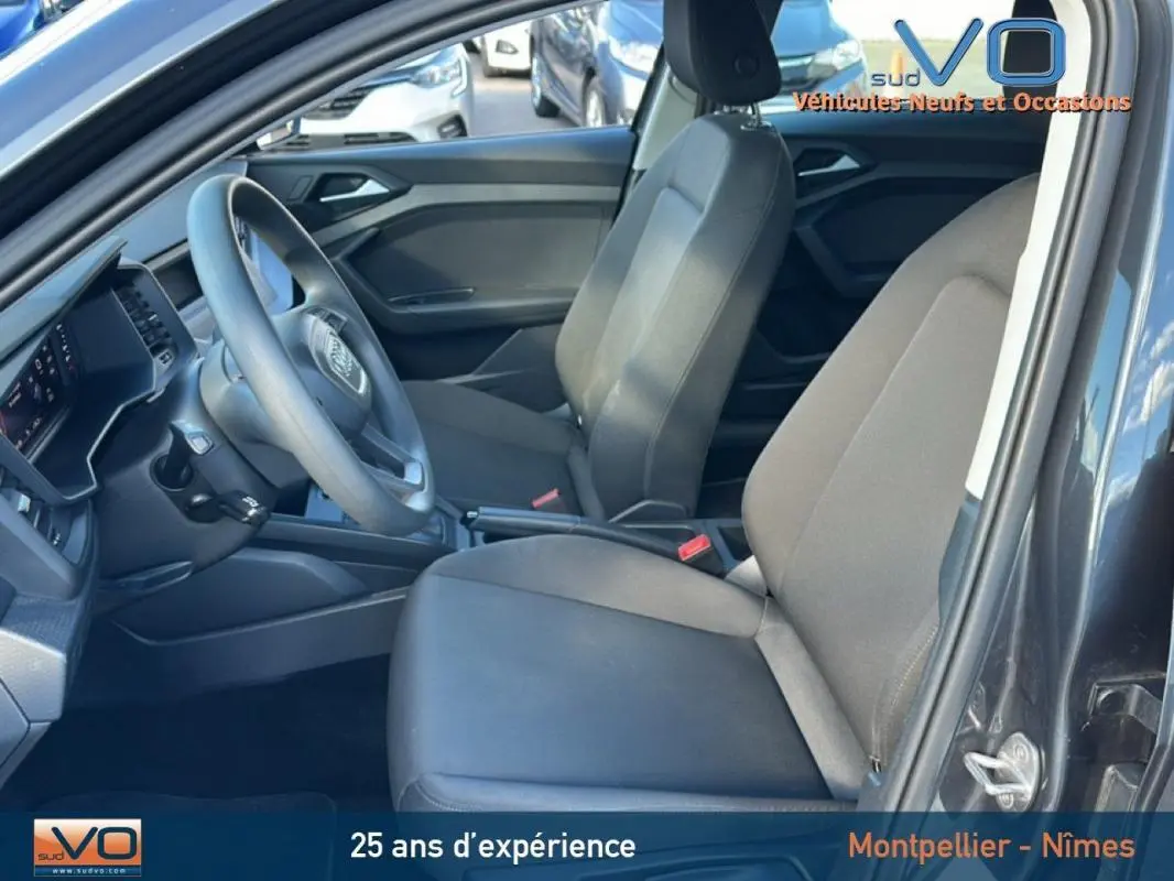 Vue intérieure côté conducteur de l'Audi A1 Sportback gris foncé, montrant sièges et tableau de bord modernes.