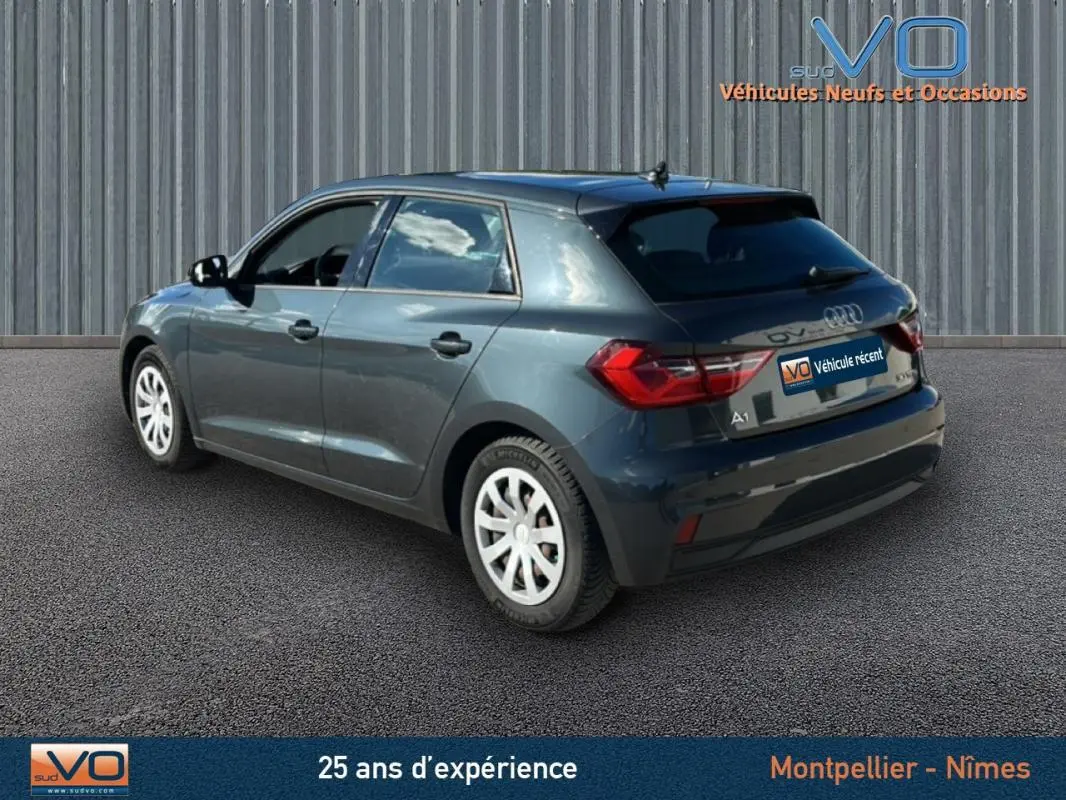 Audi A1 Sportback gris foncé vue 3/4 arrière côté gauche, avec feux arrière et jantes blanches visibles