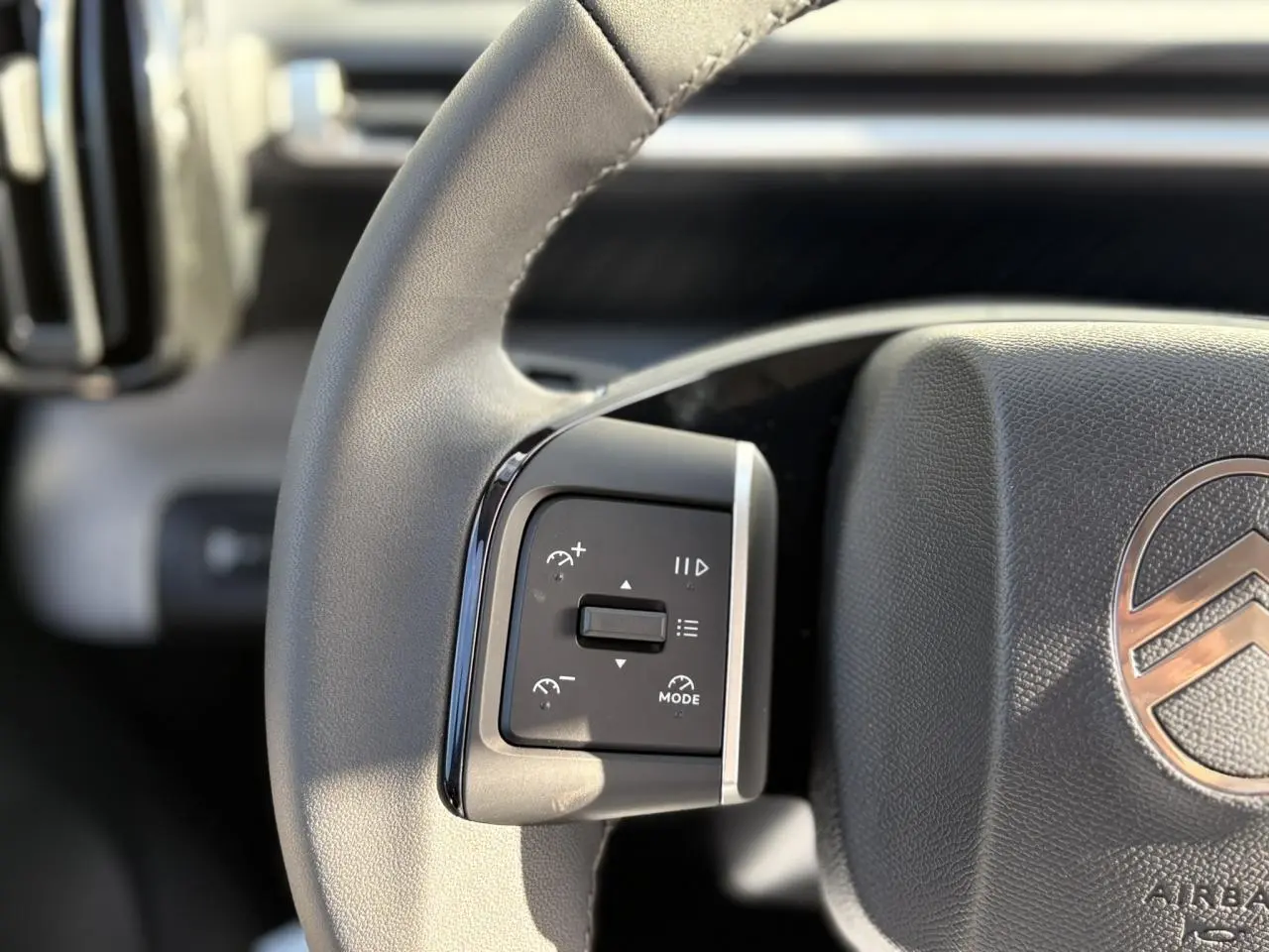 Gros plan sur le volant multifonctions gris clair du Citroën C3 Aircross Hybrid avec commandes de régulateur.