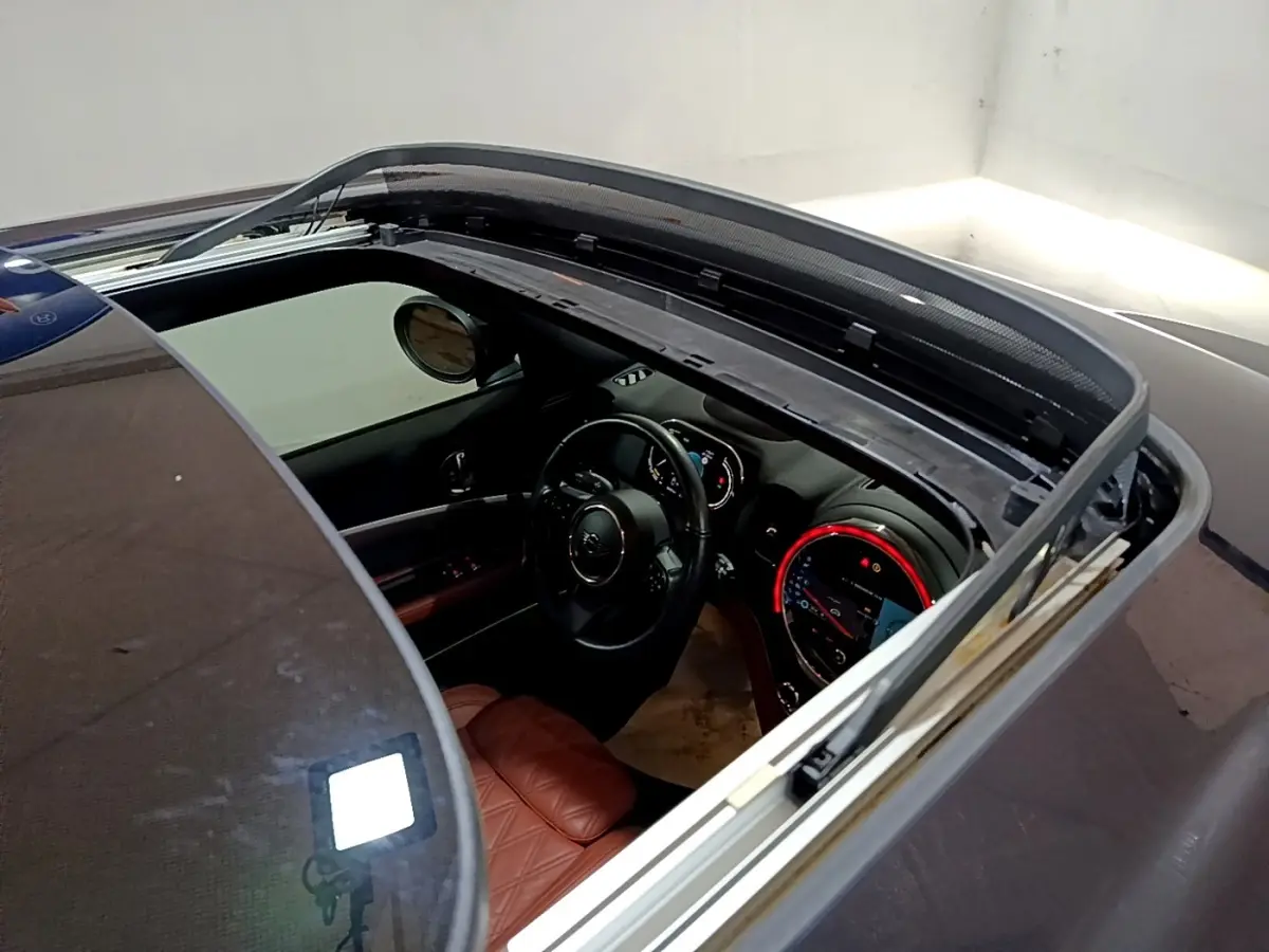 Vue plongeante sur l'intérieur d'une MINI Countryman bleu, toit ouvrant ouvert, volant cuir et tableau de bord éclairé.