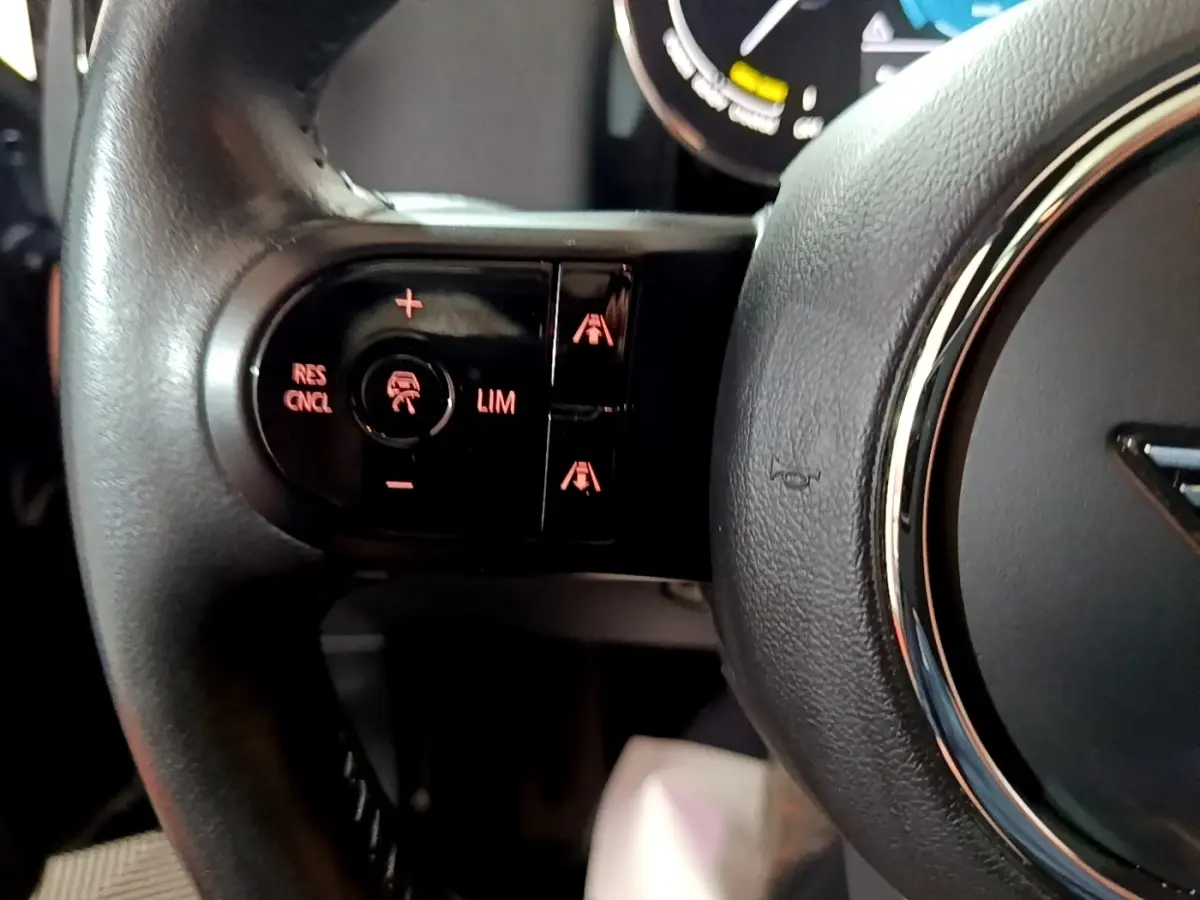 Gros plan sur les commandes de régulateur de vitesse à gauche du volant cuir du MINI Countryman Cooper SE bleu 2021.