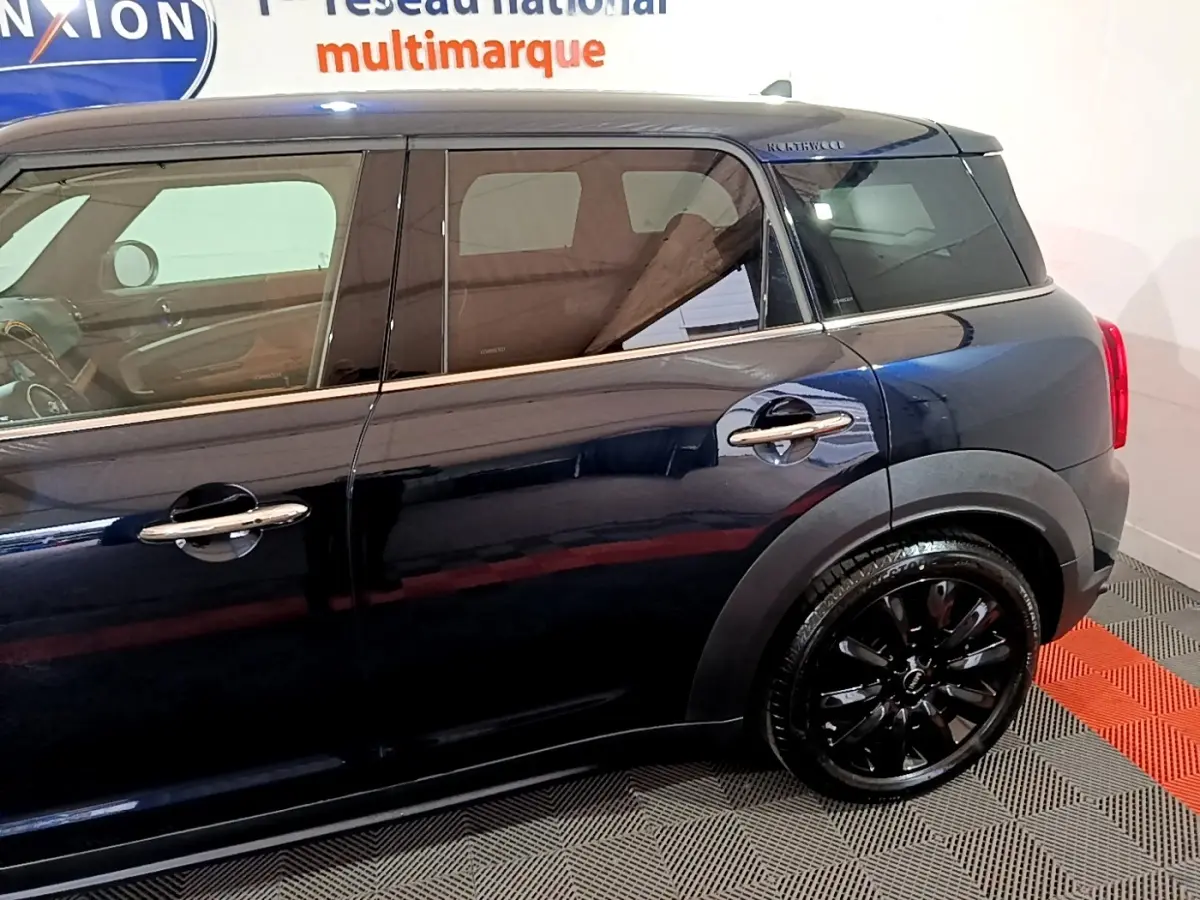 Profil côté gauche d'une MINI Countryman bleu foncé avec jantes noires brillantes dans un showroom intérieur.