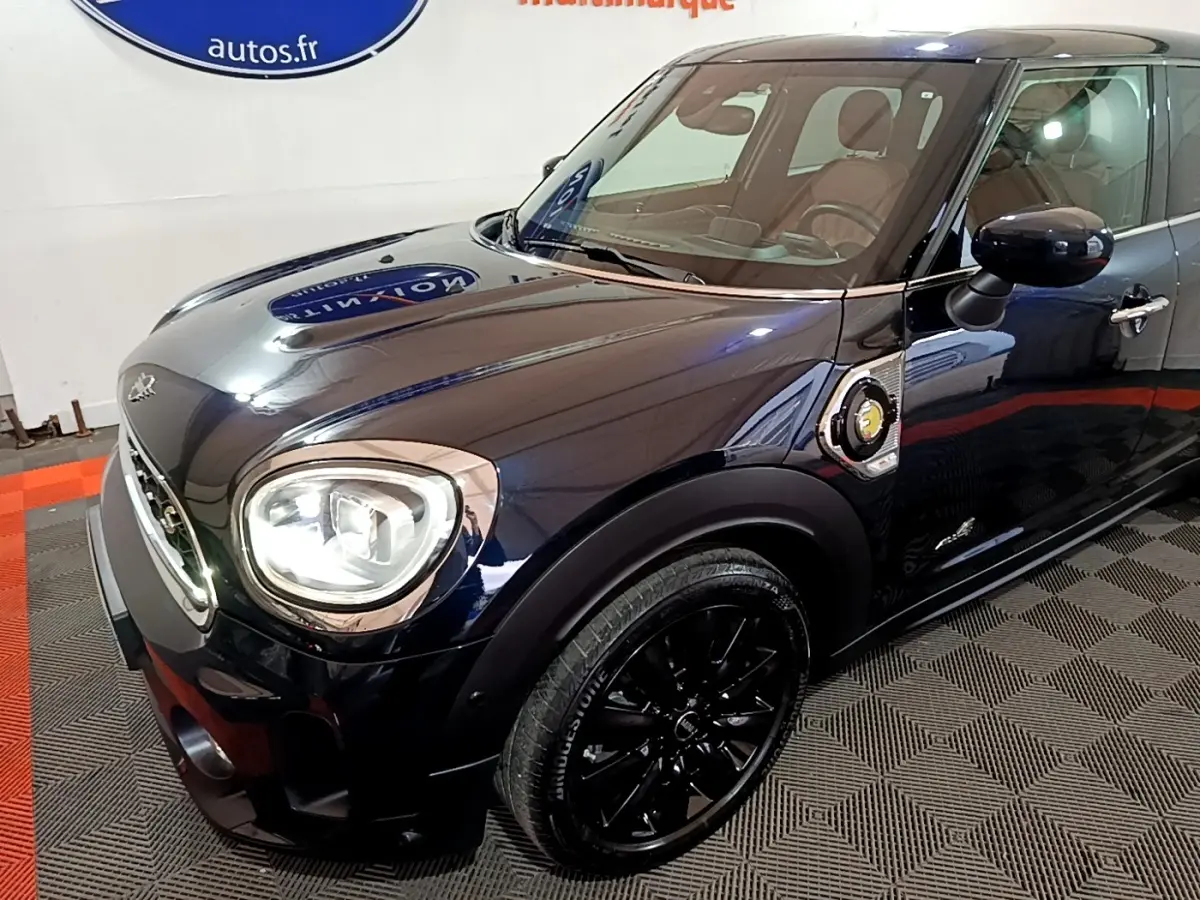 Vue 3/4 avant droit d'une MINI Countryman Cooper SE hybride rechargeable bleu foncé avec jantes noires et logo électrique sur l'aile.