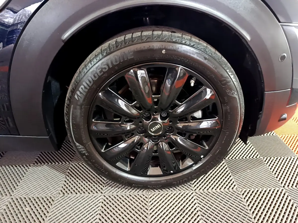 Gros plan sur la roue avant droite noire brillante du MINI Countryman Cooper SE bleu, avec pneu Bridgestone visible.