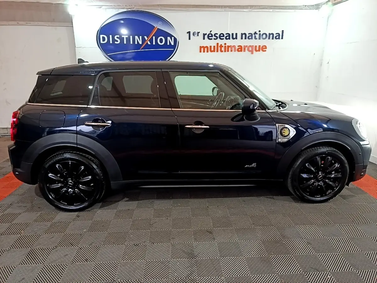 Profil droit d'une MINI Countryman Cooper SE hybride rechargeable bleu foncé avec jantes noires dans un showroom.