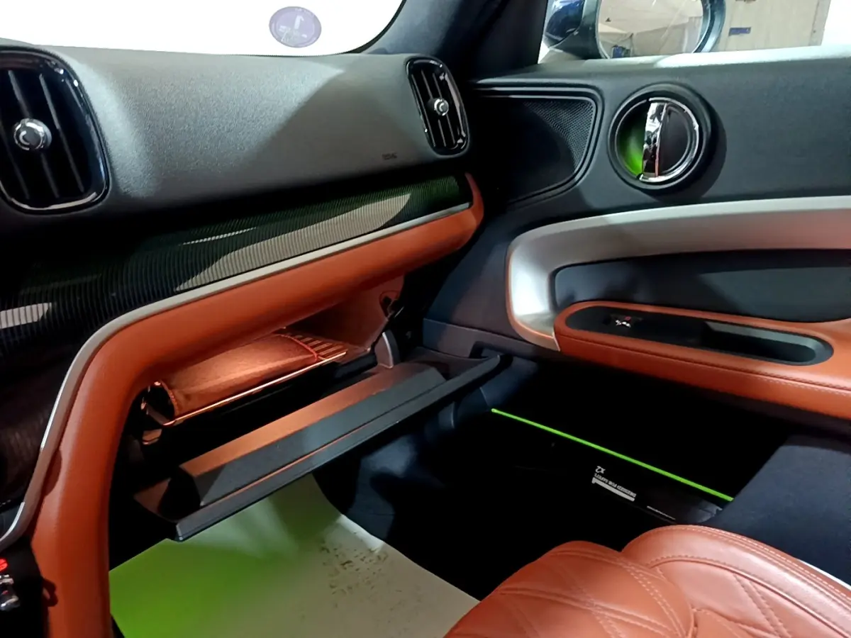 Intérieur côté passager du MINI Countryman hybride, avec garnitures cuir marron et inserts argentés sur la portière.
