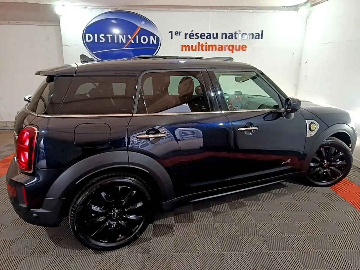 Vue latérale droite d'un MINI Countryman Cooper SE bleu avec jantes noires et toit foncé en intérieur showroom.