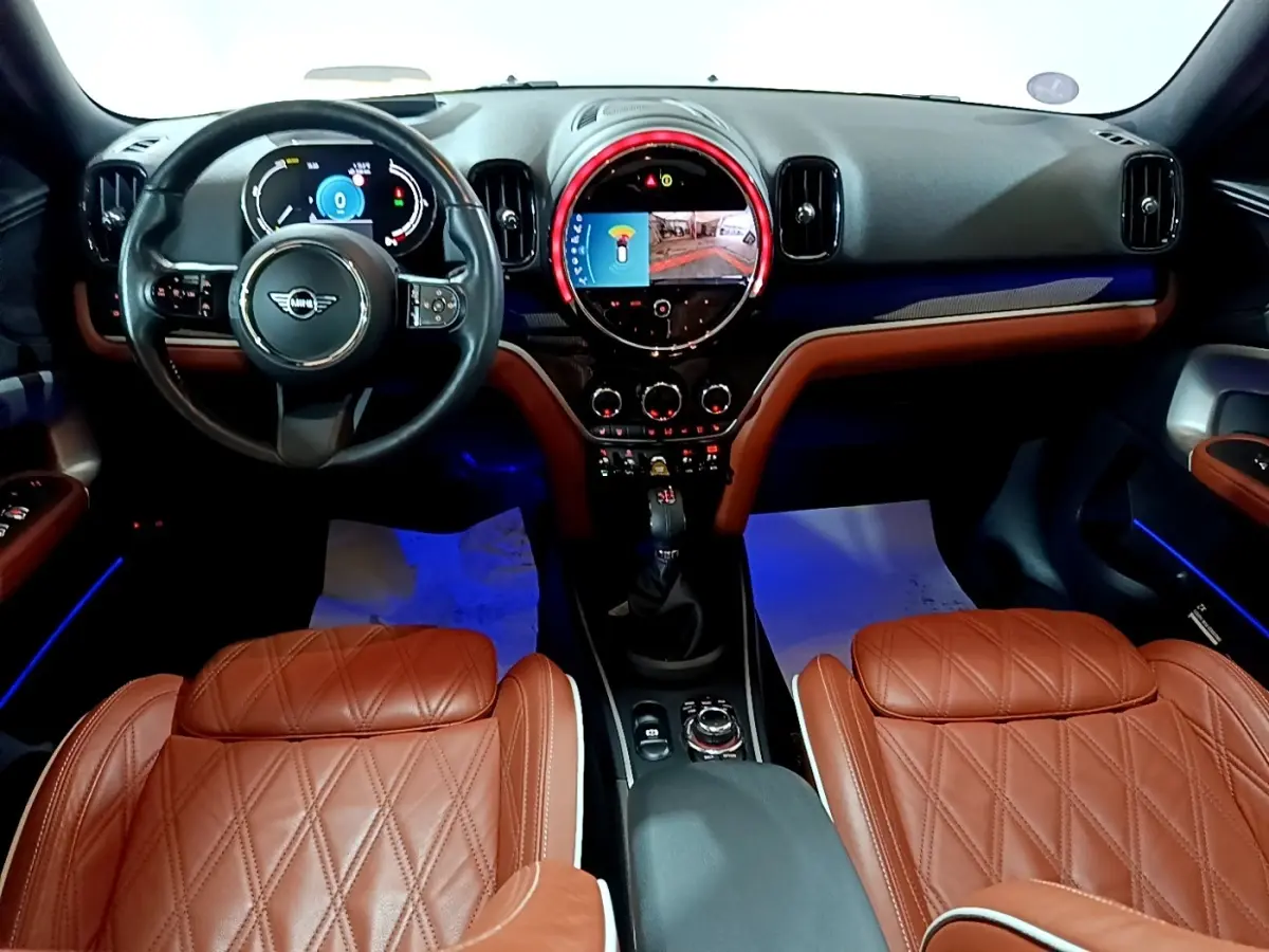 Vue intérieure avant du MINI Countryman Cooper SE avec sièges en cuir marron et tableau de bord numérique éclairé.