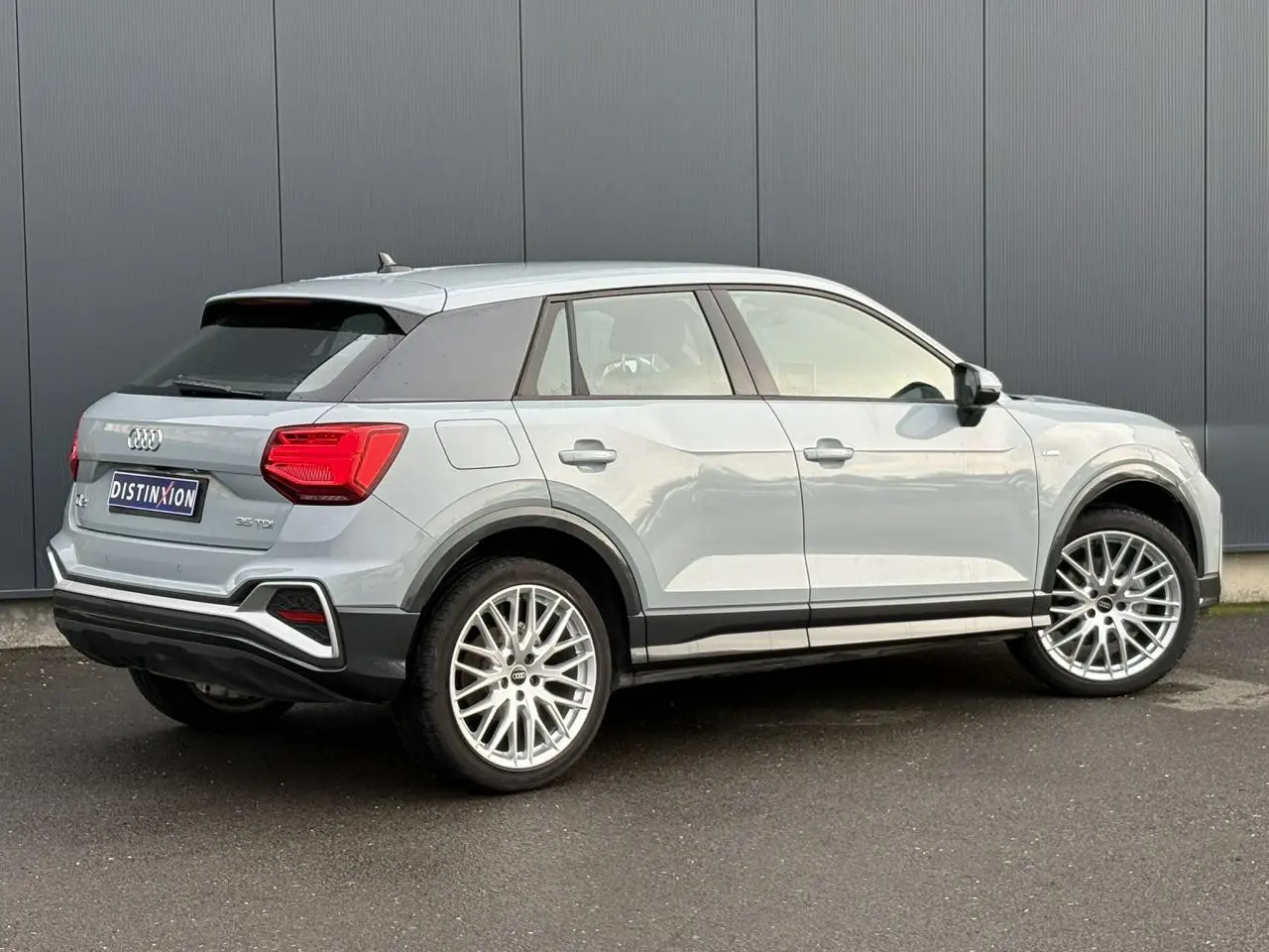 Audi Q2 35 TDI S-Line gris Flèche vue 3/4 arrière droit, avec jantes alliage et feux arrière LED distinctifs.