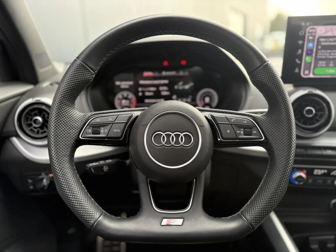 Gros plan sur le volant sport en cuir noir de l'Audi Q2 35 TDI S-Line avec commandes multifonctions et logo S.