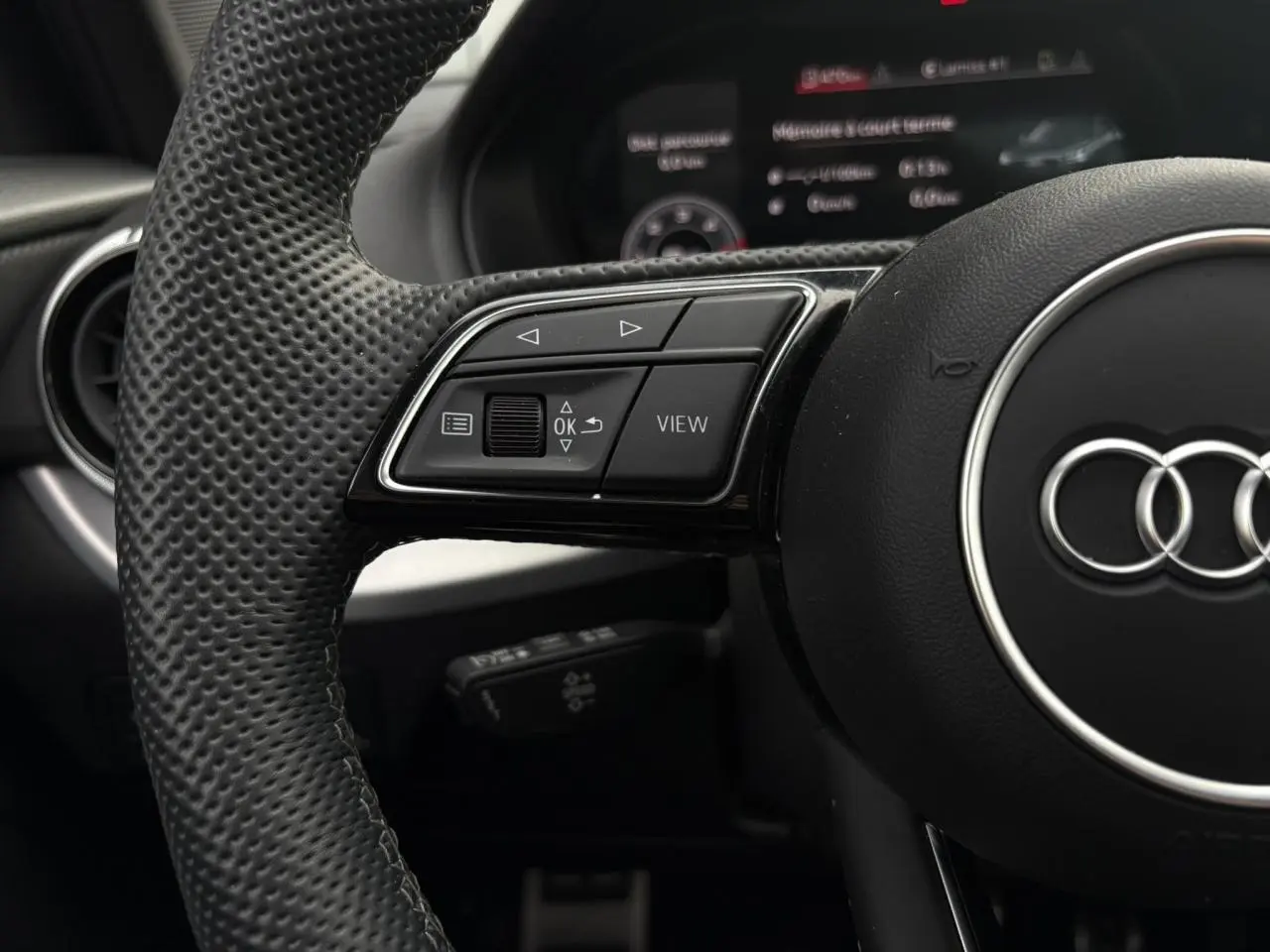 Gros plan sur le volant cuir perforé de l'Audi Q2 35 TDI S-Line avec commandes multifonctions et logo Audi central.