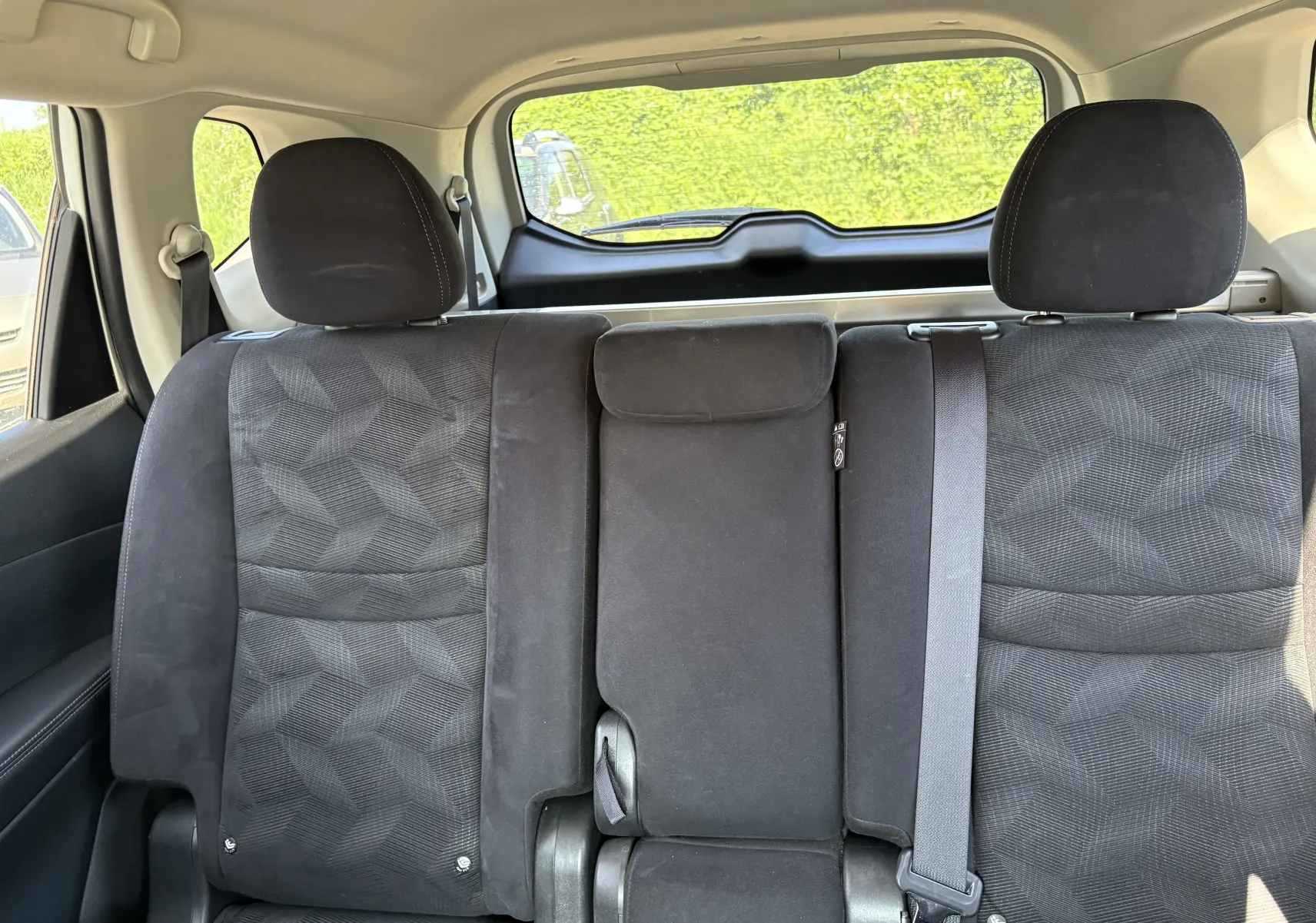 Vue intérieure arrière du Nissan X-TRAIL 2016, sièges noirs en tissu avec motifs géométriques et ceinture de sécurité visible.