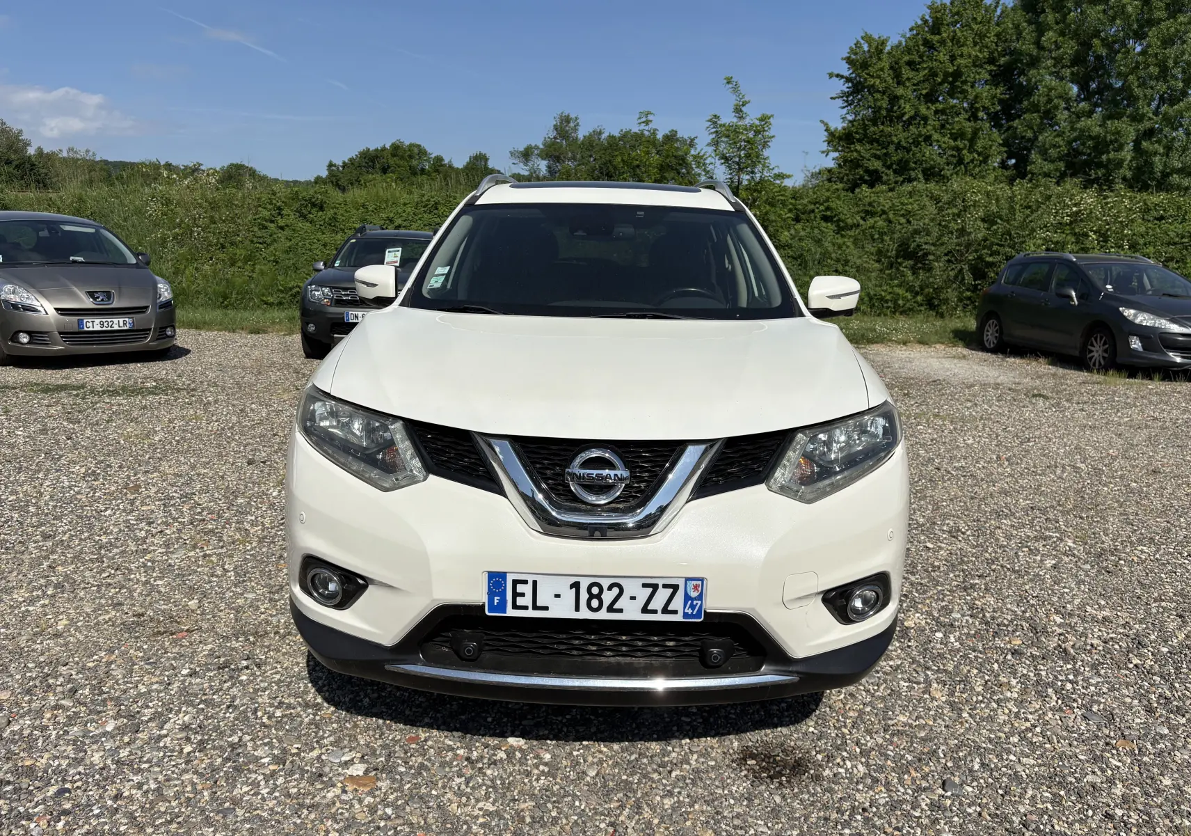 Vue de face d'un Nissan X-Trail blanc 2016, version White Edition, sur un parking extérieur sous un ciel bleu.