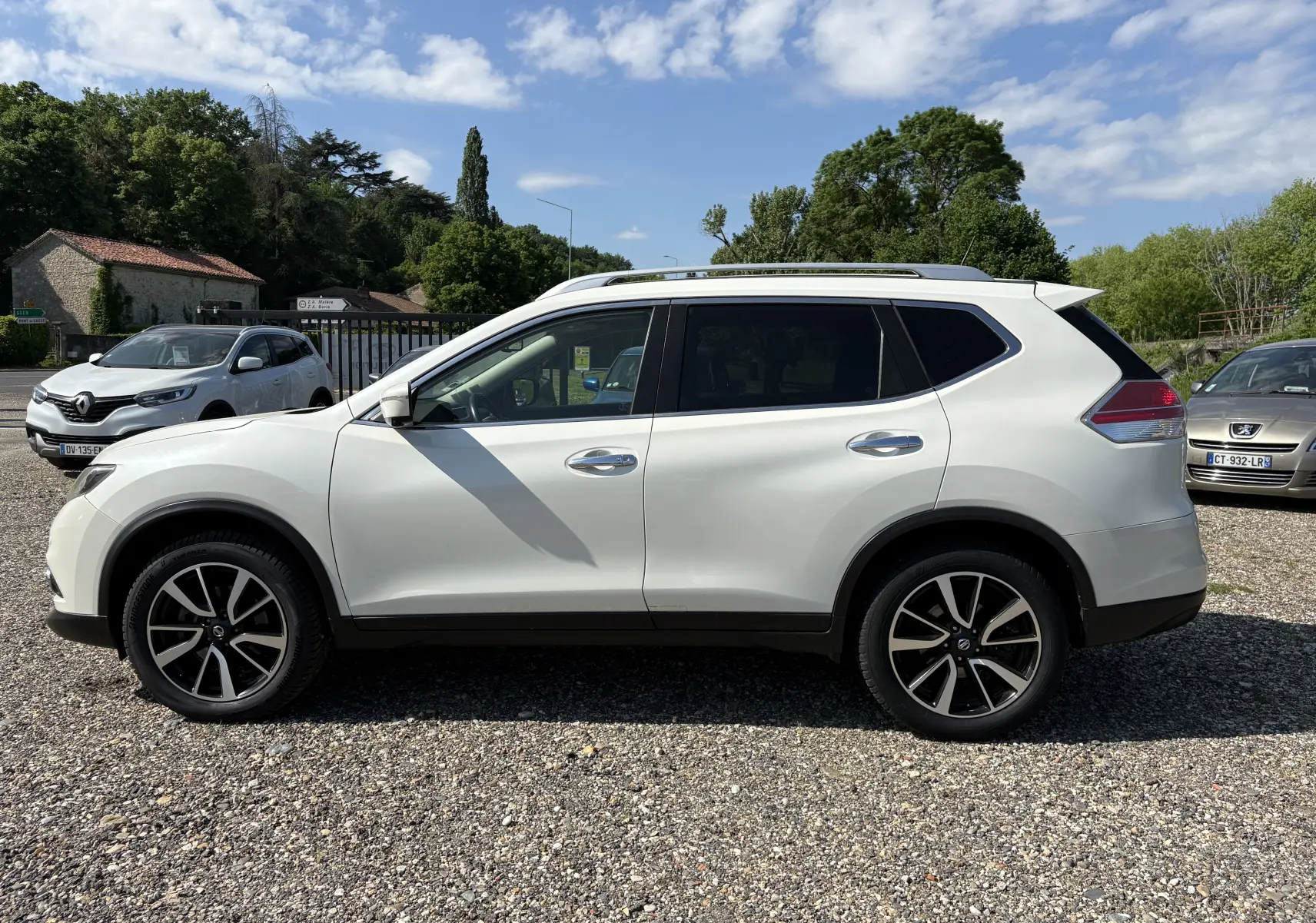 Vue de profil côté gauche d'un Nissan X-Trail 2016 blanc, version White Edition 7 places avec jantes alliage noires.