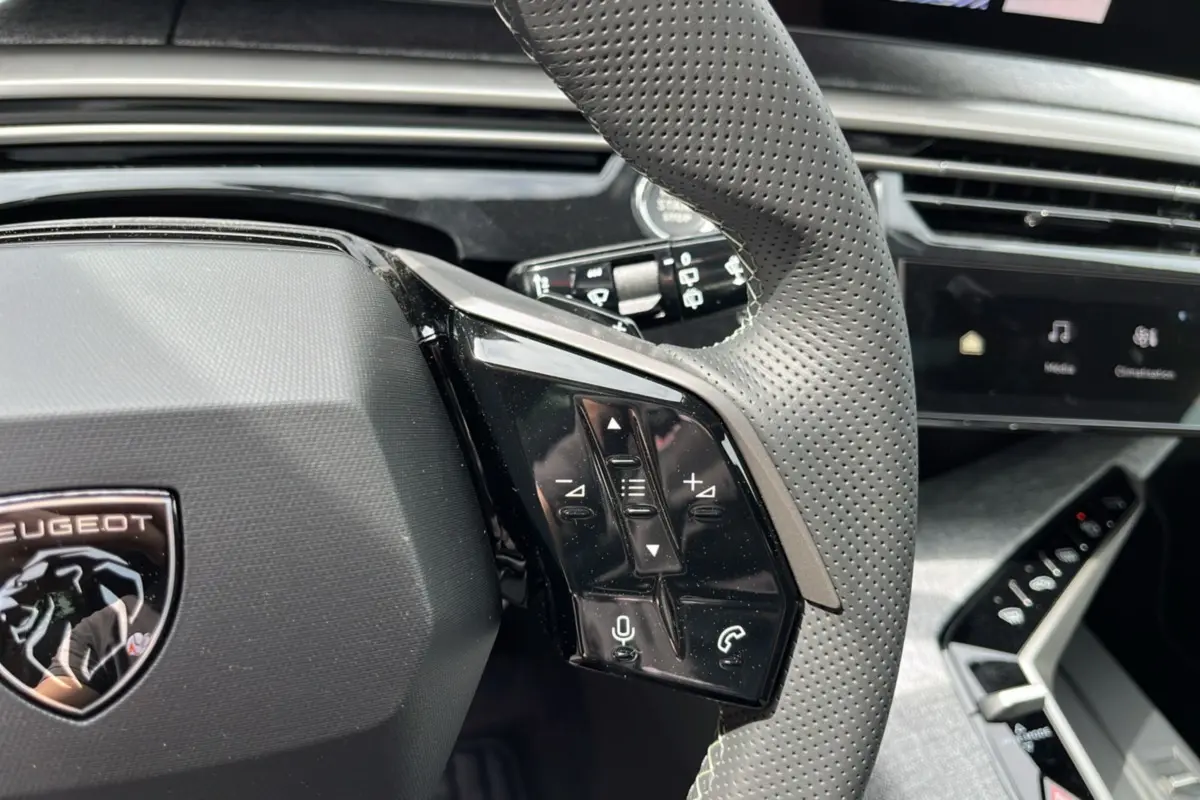 Gros plan sur le volant cuir perforé gris du Peugeot 5008 Hybrid 145 GT avec commandes multifonctions et tableau de bord digital.