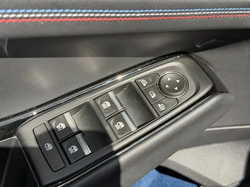 Gros plan sur les commandes des vitres électriques côté conducteur, avec surpiqûres tricolores sur la porte du Renault Rafale noir étoilé.