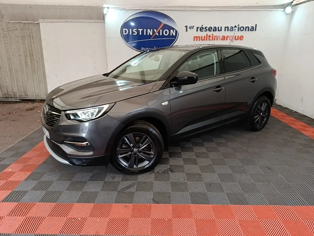 Opel Grandland X gris foncé en 3/4 avant droit, avec jantes noires et phares LED allumés, en intérieur showroom.