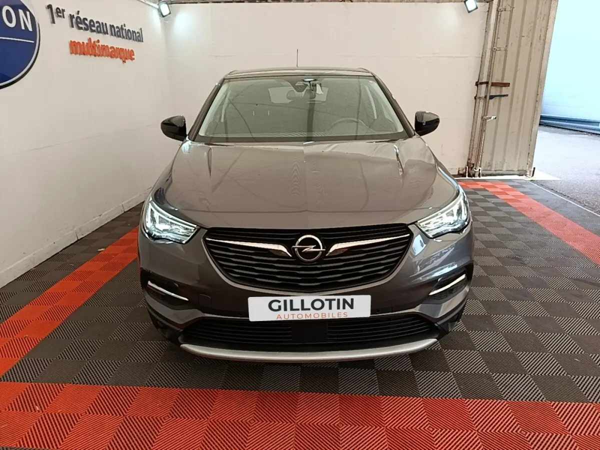 Vue frontale d'un Opel Grandland X gris foncé avec phares LED allumés, sur sol à damiers rouge et noir en intérieur.