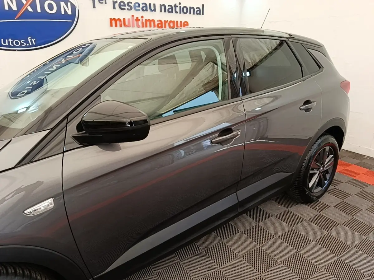 Vue côté gauche d'un Opel Grandland X gris foncé, mettant en valeur les jantes noires et les rétroviseurs noirs brillants.