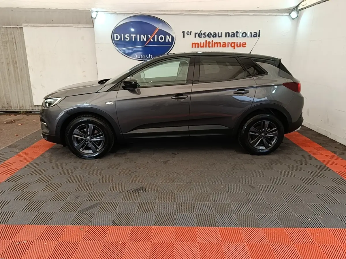 Profil côté gauche d'un Opel Grandland X gris foncé 2021 garé en intérieur avec jantes noires et toit noir.