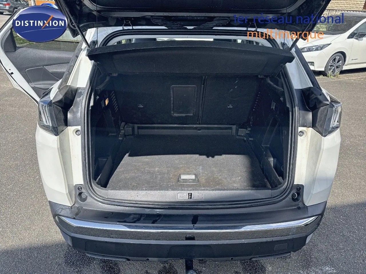 Coffre ouvert vu de l'arrière d'un Peugeot 3008 blanc nacré 2022 avec attelage visible sur parking.