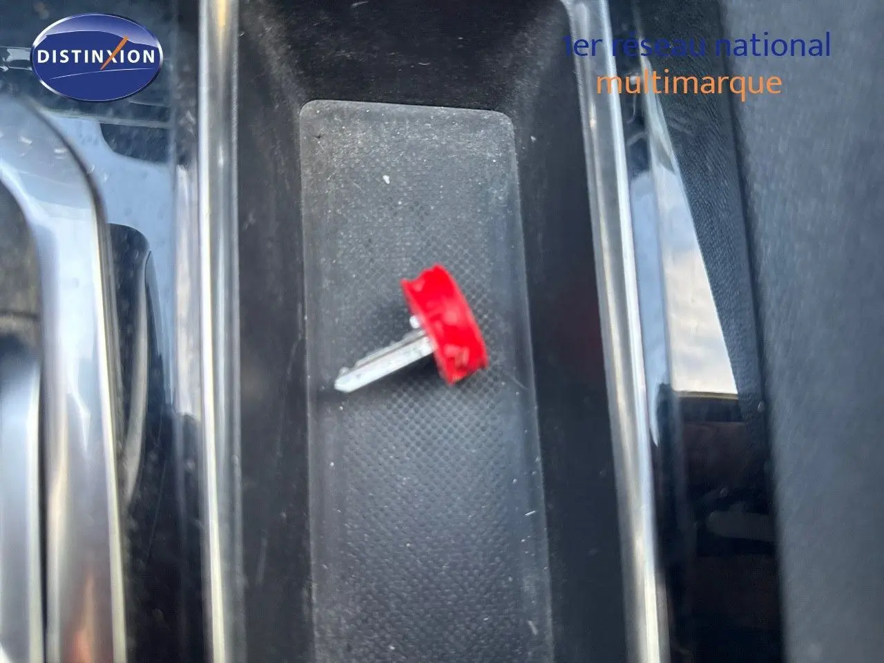 Gros plan sur la console centrale noire d’un Peugeot 3008 blanc nacré, avec une clé rouge posée dessus.