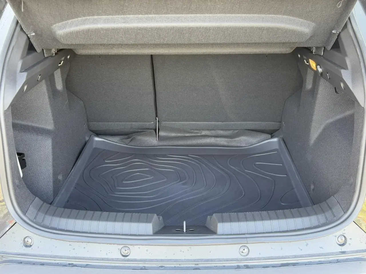 Coffre ouvert du Dacia Duster noir nacré 2025, montrant le tapis de coffre et l'espace de rangement intérieur.