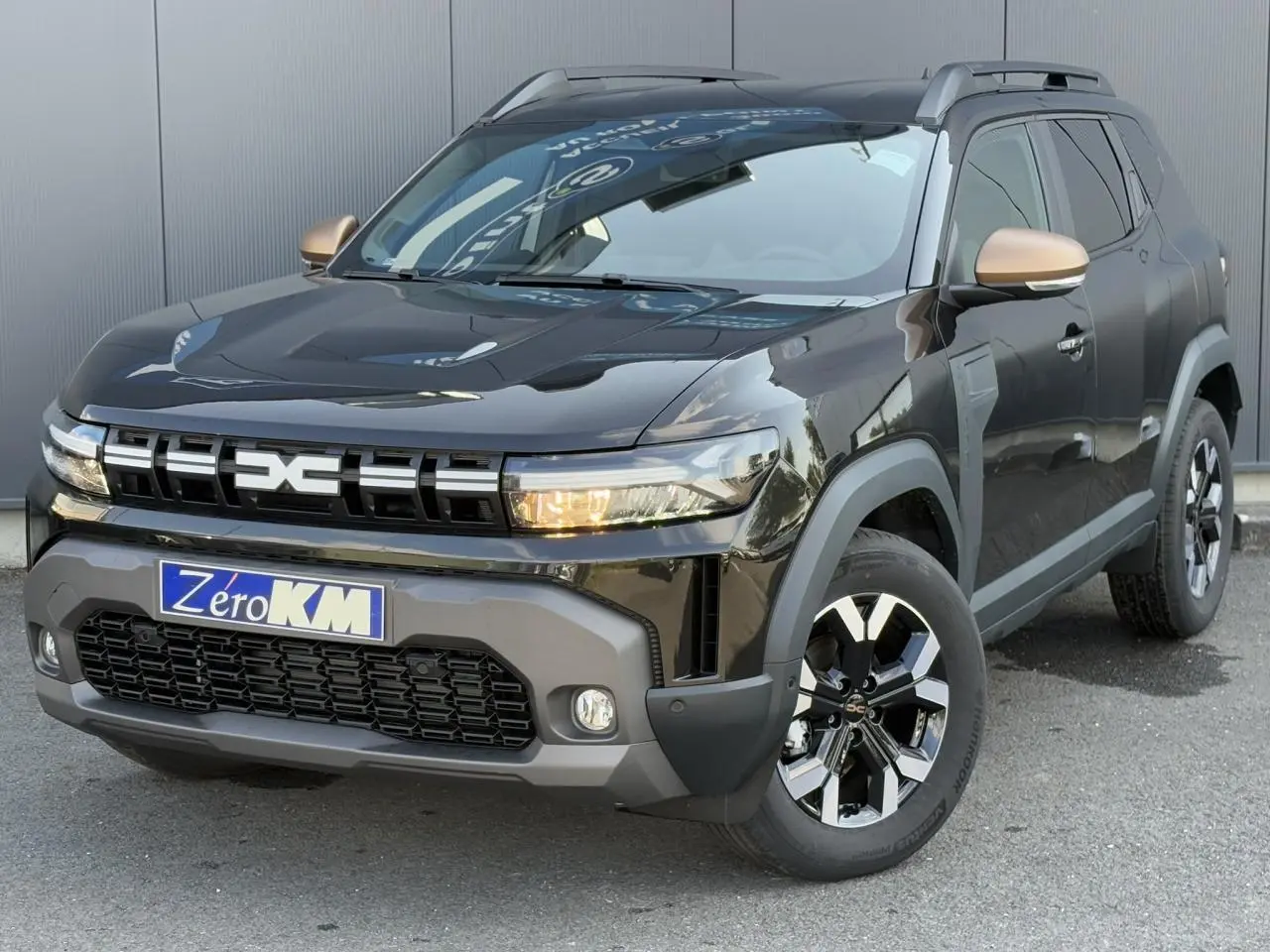 Vue 3/4 avant d'un Dacia Duster 2025 noir nacré avec coques de rétroviseurs brun cuivré et jantes alliage 17 pouces.