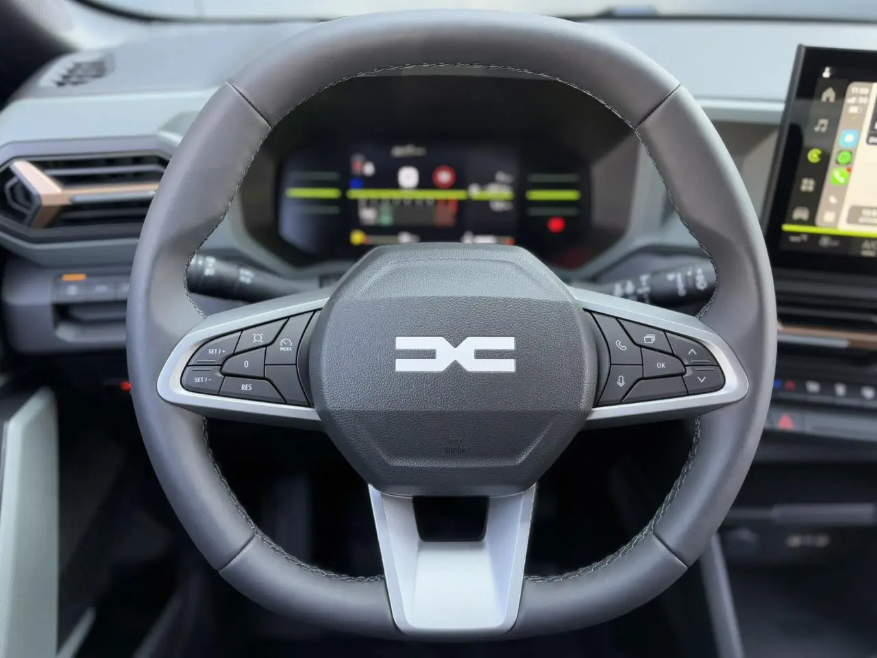 Volant noir du Dacia Duster 2025 TCE 4X2 Mild Hybrid avec commandes intégrées et tableau de bord digital en arrière-plan