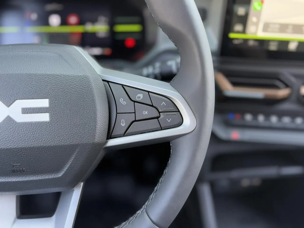 Gros plan sur le volant gris du Dacia Duster 2025 avec commandes intégrées et tableau de bord flou en arrière-plan.