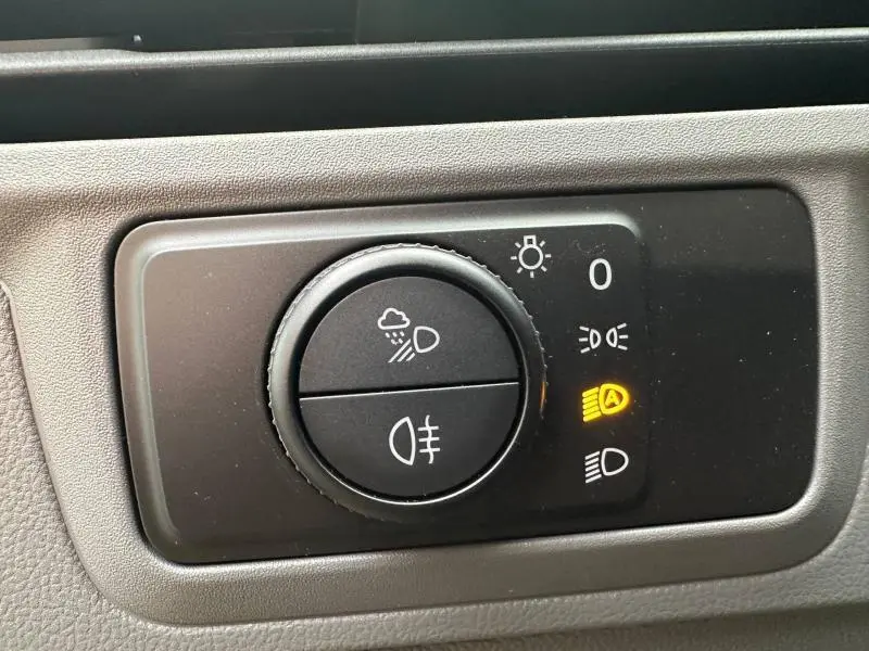 Gros plan sur le bouton de commande des phares avec indicateur allumé dans un Volkswagen Transporter FGN gris 2025.