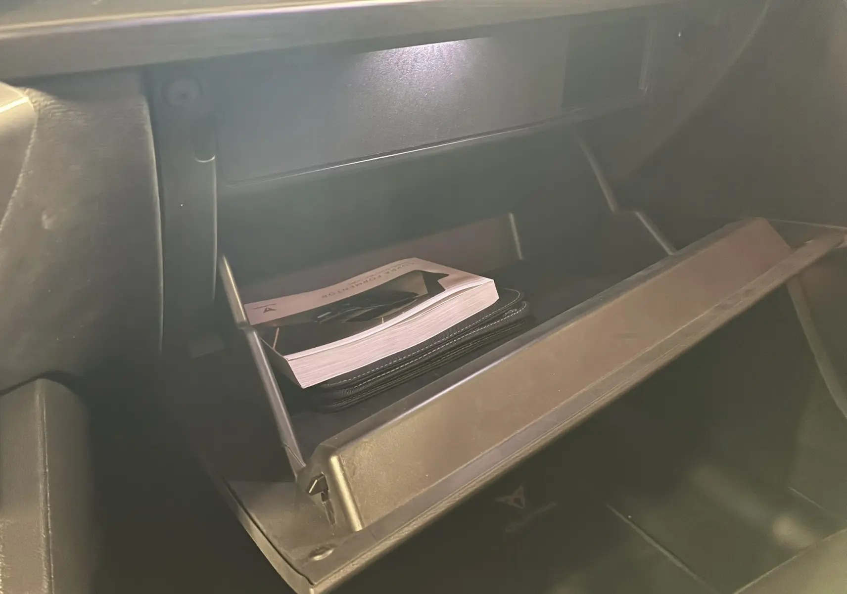 Vue rapprochée de la boîte à gants ouverte du CUPRA Formentor gris avec manuel et pochette à l'intérieur.