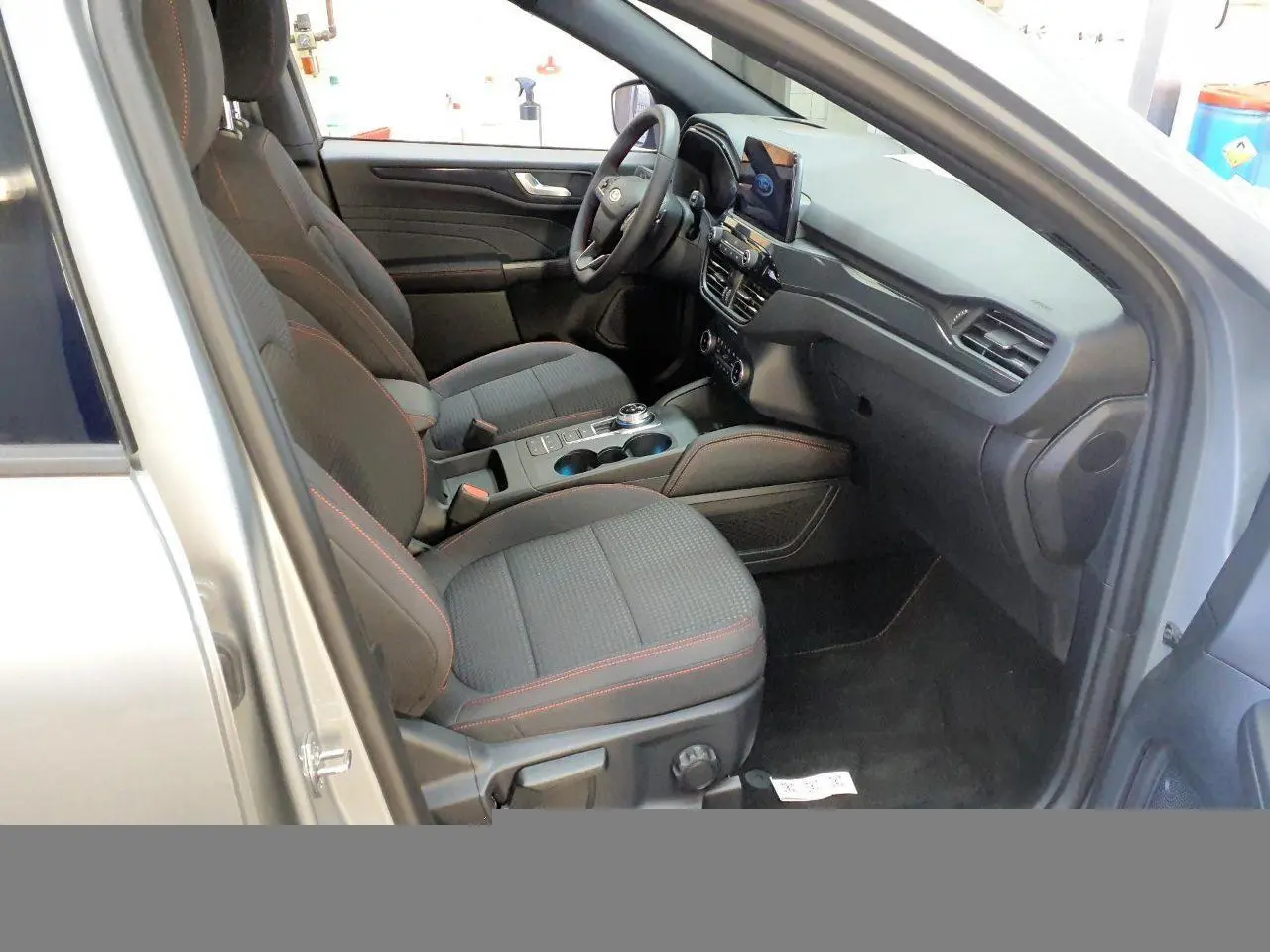 Vue intérieure côté conducteur du Ford Kuga gris Solar 2024, sièges tissu avec surpiqûres rouges et tableau de bord moderne.