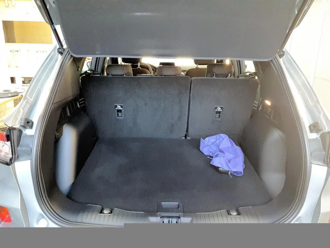 Vue arrière du coffre ouvert d'un Ford Kuga gris Solar 2024, avec banquette arrière relevée et un tissu violet posé.