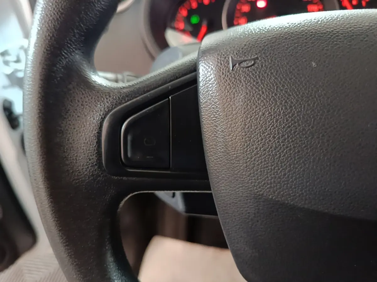 Gros plan sur le volant noir du Renault Kangoo 2020 avec commandes intégrées et tableau de bord en arrière-plan flou.