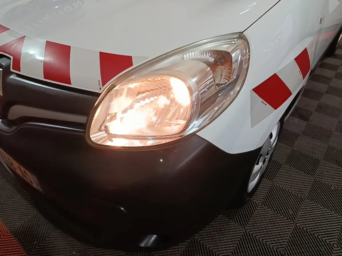Gros plan sur l'avant droit du Renault Kangoo blanc avec phare allumé et bandes rouges réfléchissantes.