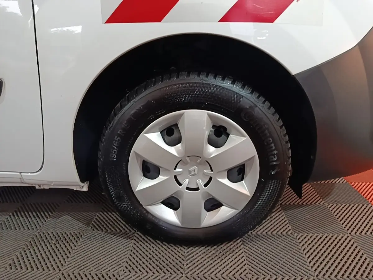 Gros plan sur la roue arrière droite blanche d’un Renault Kangoo avec enjoliveur argenté et marquage rouge sur la carrosserie.