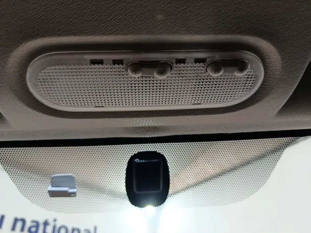 Vue intérieure en gros plan du plafonnier gris avec interrupteurs et capteur sur le pare-brise du Renault Kangoo blanc.