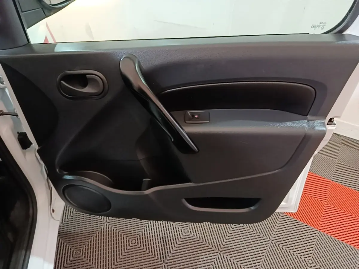 Vue rapprochée de la porte avant gauche noire du Renault Kangoo blanc, avec poignée intérieure et haut-parleur intégré.