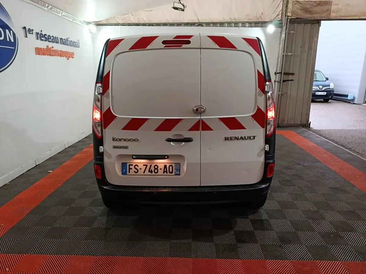 Vue arrière d’un Renault Kangoo blanc avec bandes réfléchissantes rouges et blanches, feux arrière allumés en intérieur.