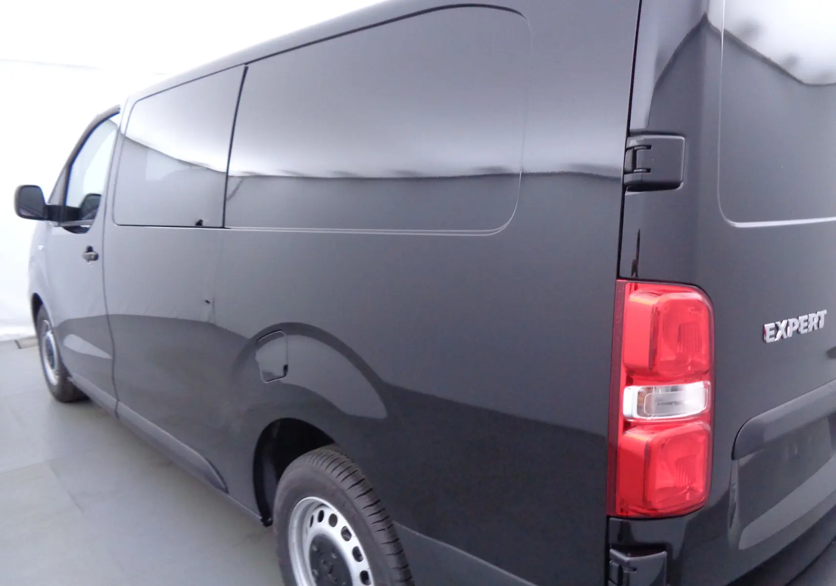 Vue 3/4 arrière droite d'un Peugeot Expert Cabine Approfondie noir perle métal, fourgon utilitaire sans vitres latérales.