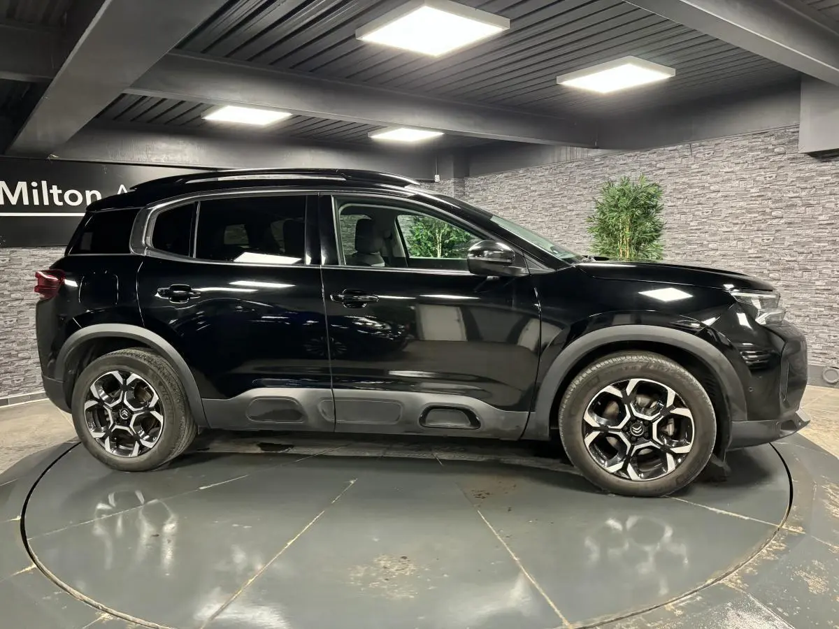 Profil côté gauche d'un SUV Citroën C5 Aircross noir nacré avec jantes alliage bi-ton et barres de toit noires.