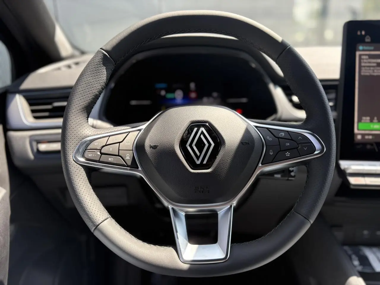 Volant cuir multifonctions noir avec logo Renault au centre, tableau de bord et écran tactile du Captur hybride 2025 visibles en arrière-plan.