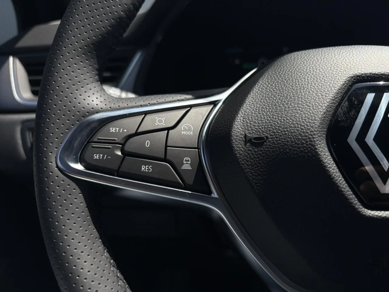 Gros plan sur le volant cuir perforé de la Renault Captur 2025, avec commandes du régulateur adaptatif côté gauche.