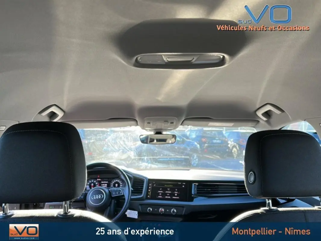 Vue intérieure arrière montrant le tableau de bord et le volant cuir d'une Audi A1 Sportback gris foncé de 2019.