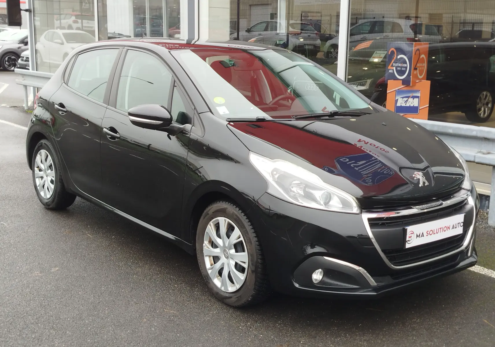 Peugeot 208 noire vue en 3/4 avant droit, avec jantes argentées et calandre chromée brillante.