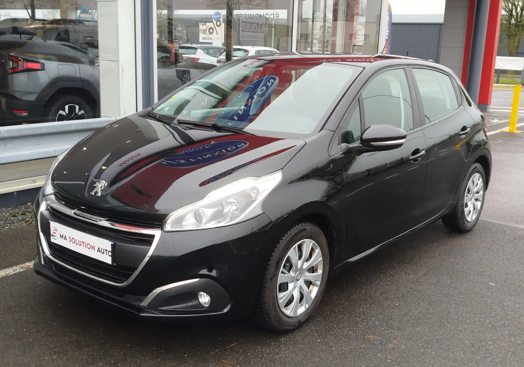 Peugeot 208 noir Perla Nera vue 3/4 avant droit, avec phares allumés et jantes alliage visibles.