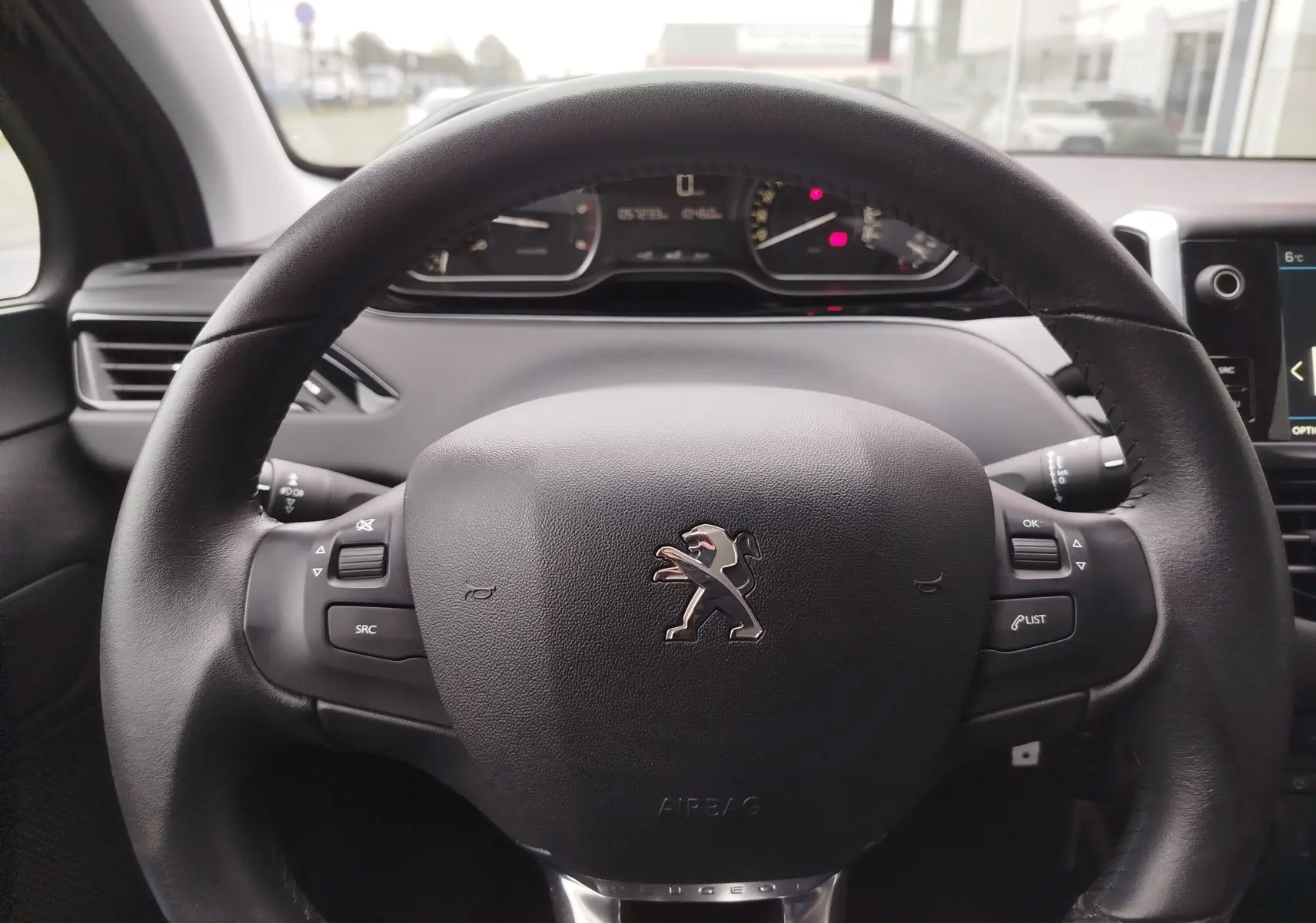 Vue rapprochée du volant noir de la Peugeot 208 2019 avec commandes intégrées et tableau de bord en arrière-plan flou.