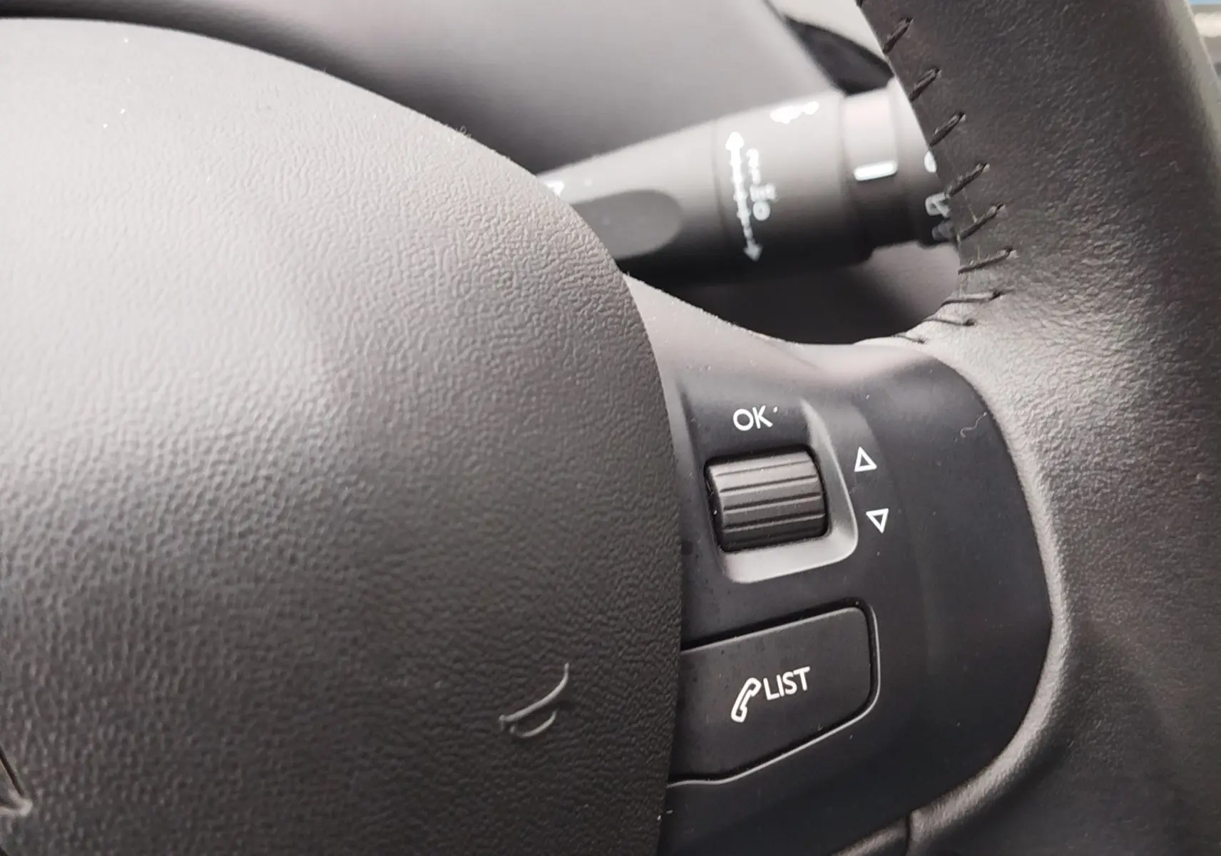 Gros plan sur les commandes au volant en cuir noir de la Peugeot 208, avec boutons OK et LIST visibles.